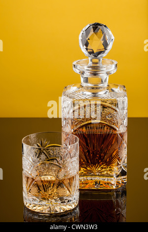 Crystal Whiskey glass and bottle isolated on dark yellow background Stock Photo