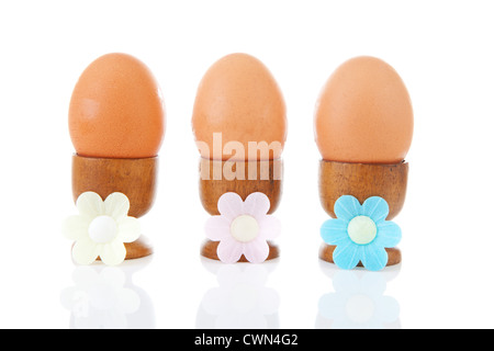 Three chicken eggs in a row in wooden holders over white background Stock Photo