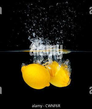 Two fresh lemons falling into water, isolated on black background Stock Photo