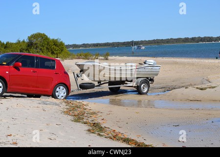 Red Suzuki swift backing boat trailer into water across the beach Stock Photo