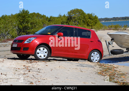 Red Suzuki swift backing boat trailer into water across the beach Stock Photo