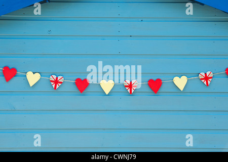 Wooden Union Jack heart shapes strung up on a blue garden shed. England Stock Photo