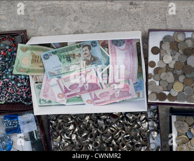 coins, rings beads bracelets in marked stall with old banknotes from Iraq picturing Saddam Hussein in the middle Stock Photo