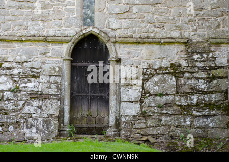 An old, wooden, oak door, blackened with aged and decorated with wrought iron features, set in the old stone wall of a 13th, 14t Stock Photo