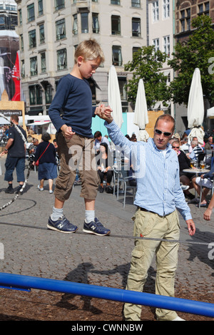 Young boy balancing and tightrope walking on a wire with a firm grip in his father's hand at the pedestrian street Stroeget, (Strøget), Copenhagen Stock Photo