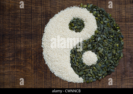The yin yang created out of pumpkin seeds and sesame seeds on a dark wood surface Stock Photo