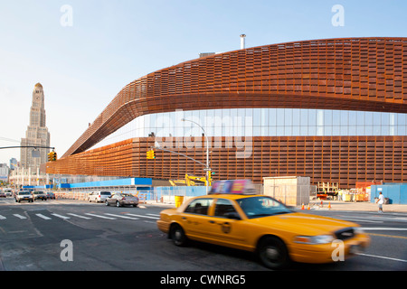 New York City Taxi drives pass the new Barclays Center home of the Brooklyn Nets Sports Arena and Concert Hall.  The landmark Williamsburgh Savings Bank Tower in the background, Brooklyn, NY, USA Stock Photo