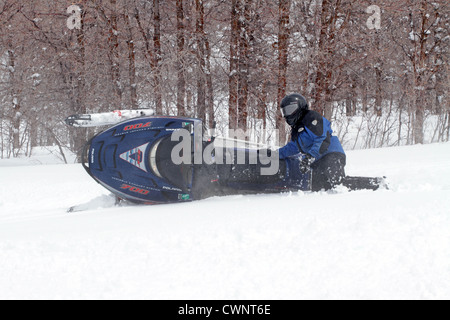 Snowmobile rider having fun and turning in fresh white snow. Sharp turns result in an overturned snowmobile. Stock Photo