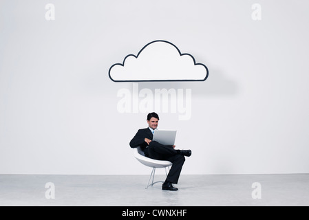Businessman using laptop computer beneath cloud representing cloud computing Stock Photo