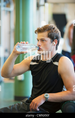 Young man drinking bottled water in gym room Stock Photo