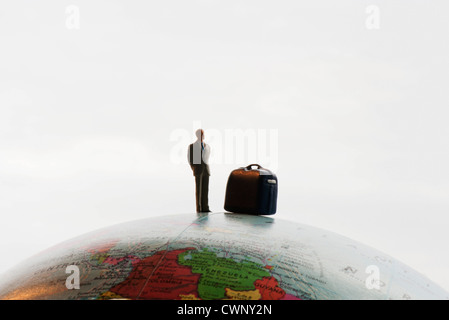 Businessman figurine with luggage standing on top of globe Stock Photo