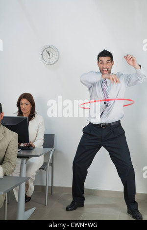 Young businessman playing with hula hoop in office while colleagues work Stock Photo