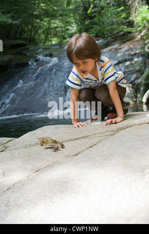 Boy crouching on rock looking at frog jump Stock Photo