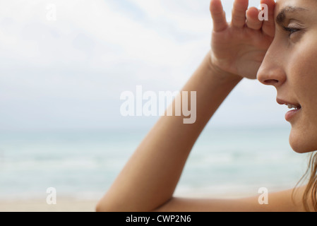 Woman at the beach, shading eyes and looking away Stock Photo