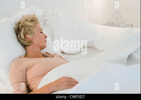mature woman in pajama lying down sleeping in a hotel bed with her feet