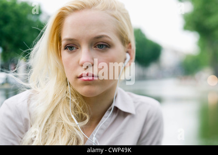 Young woman listening to earphones, looking away in thought