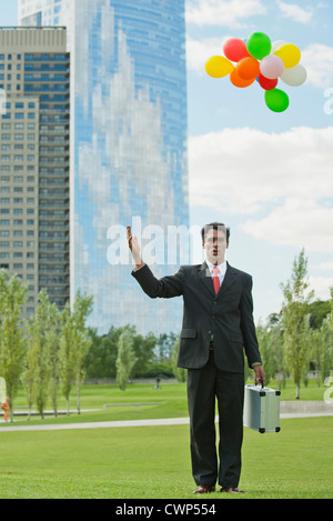 Businessman releasing bunch of balloons into air, looking disappointed Stock Photo
