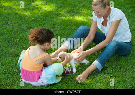 Mother and daughter sitting on grass playing with beagle puppy Stock Photo