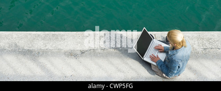 Young woman sitting beside canal, using laptop computer Stock Photo
