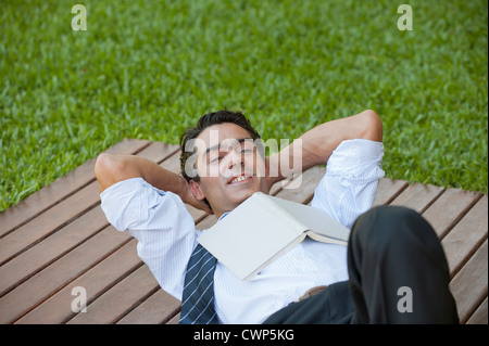 Mid-adult man lying outdoors with hands behind head and book on chest Stock Photo