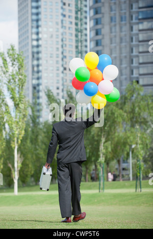 Businessman walking with bunch of balloons, rear view Stock Photo