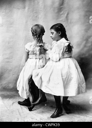 The Sisters - Two girls seated, one looking at braided hair of the other, circa 1900 Stock Photo