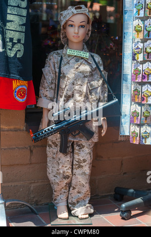 A display of a child life size doll, dressed in camouflage uniform and toy machine gun at the entrance to a souvenir shop in San Stock Photo