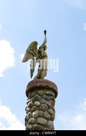 Angel holding torch on cloudy sky background. Statue on platform made of stones. Stock Photo