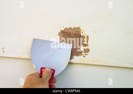 scraping old paint from siding with a putty knife in preparation for painting Stock Photo