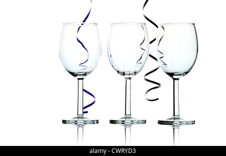 Three empty wine glasses and party streamers back lit against white background - abstract. Stock Photo