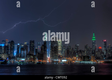 A forked lightning bolt illuminates the night sky behind the midtown skyline during a summer thunderstorm in New York City. Stock Photo
