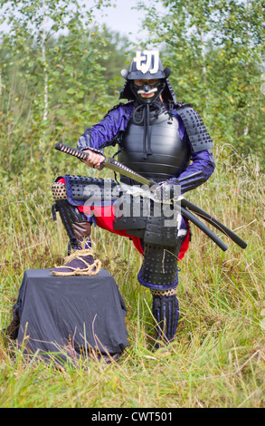 Man in Japanese medieval samurai armor (tosei-gusoku) pulling out katana sword Stock Photo