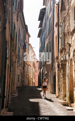 A pretty young woman walking in a street of tall houses on a sunny day in Callas, Provence France Stock Photo