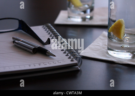 A table containing two empty drinks glasses and an open diary with a pen and spectacles on top Stock Photo