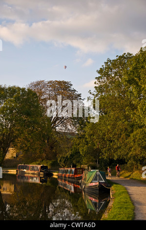 People cycling on towpath of Kennet and Avon Canal as a hot air balloon floats above Stock Photo