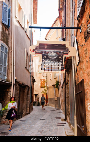 A street scene in Bargemon Provence, France with a well dressed woman walking past an Olivetti Typewriter sign for a museum Stock Photo