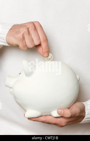 Hand putting 2 euro coin to piggy bank Stock Photo - Alamy