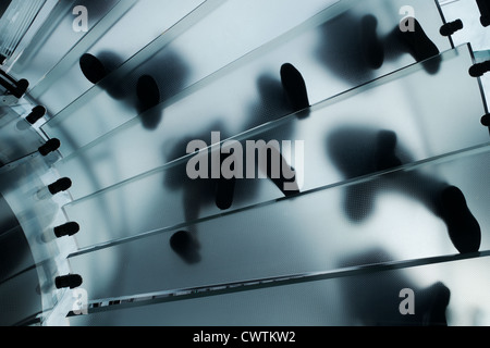 Feet walking on a glass staircase in the Apple NYC Fifth Avenue store. Feet are seen from underneath so silhouetted Stock Photo