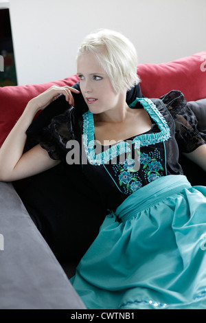 Young woman on couch wearing a dirndl Stock Photo