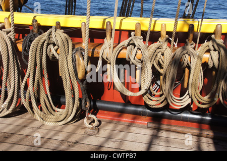 Coiled rope lines stored on belaying pins on a wooden tall ship  Stock Photo