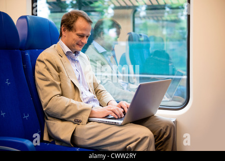 Businessman, traveling with a laptop on his lap in a train, commuting to and from work. Stock Photo