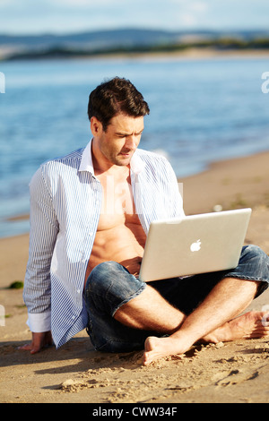 Man relaxing on beach with laptop Stock Photo