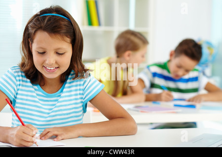 Portrait of lovely girl drawing at workplace with schoolmates on background Stock Photo