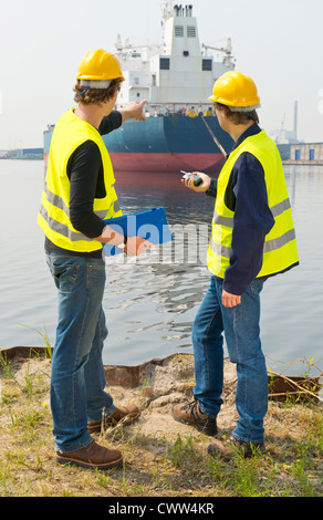 Two harbor engineers, or dockers, in discussion over a large industrial oil tanker Stock Photo