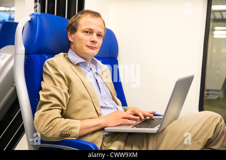 Man, wearing a suit without tie is working in a train, looking up from his laptop Stock Photo