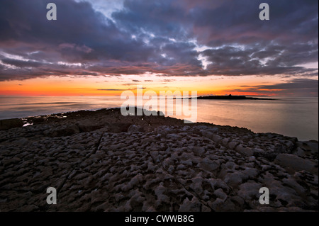 Sun setting over beach rock formations Stock Photo