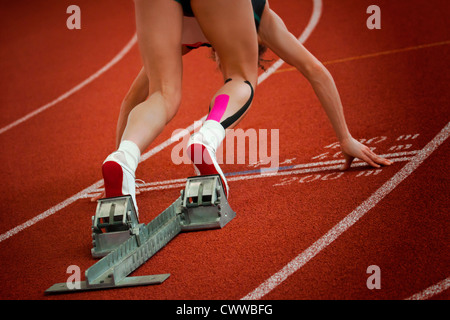 Female short distance runner on gravity slope curve is in start position Stock Photo