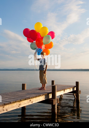 Boy holding balloons on wooden pier Stock Photo