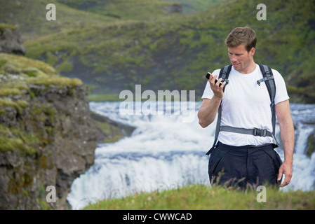 Hiker using cell phone on hillside Stock Photo