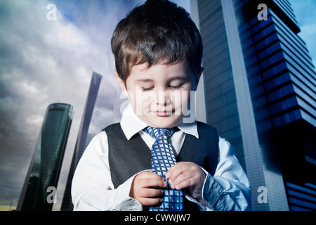 child dressed businessman with hands in his tie and skyscrapers in the background Stock Photo